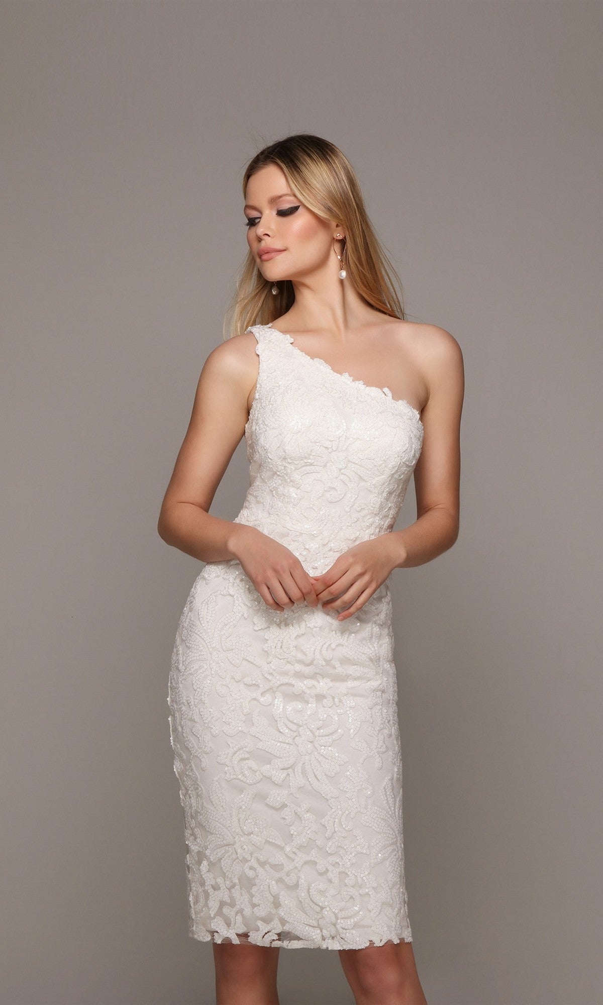 A woman stands against a neutral background wearing the Knee Length White Party Dress: Alyce 70029—a stylish one-shoulder lace dress perfect for any cocktail event.